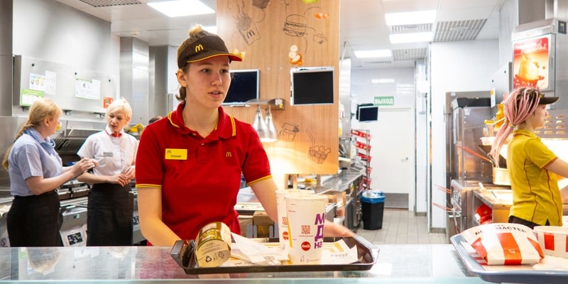Las empleadas de un restaurante de comida rápida preparan y entregan los pedidos a los clientes.