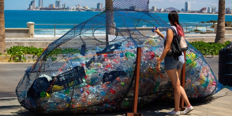 Una mujer deposita un envase de plástico en un contenedor para ser reciclado.